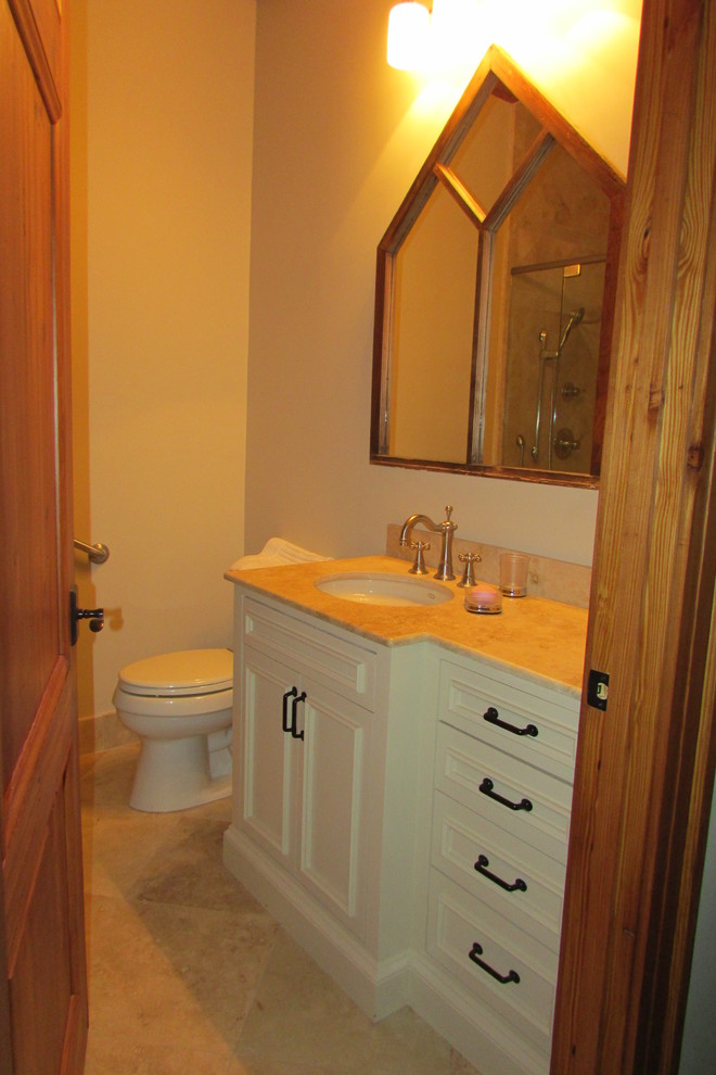 Rustik inredning av ett badrum, med ett undermonterad handfat, luckor med profilerade fronter, vita skåp, granitbänkskiva, beige kakel, vita väggar och klinkergolv i porslin