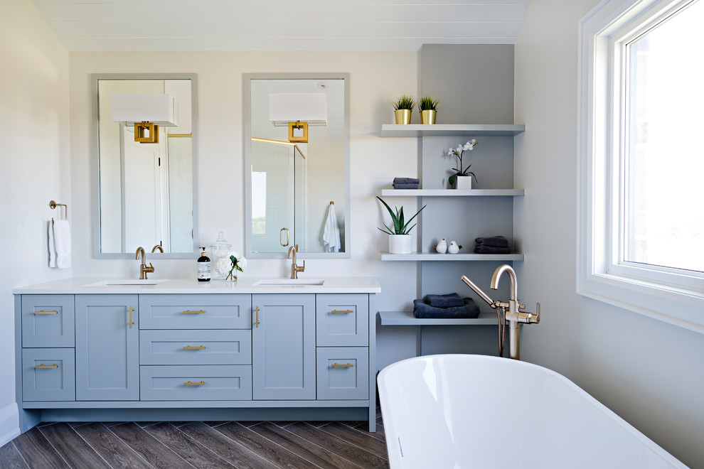 Imagen de cuarto de baño principal de estilo de casa de campo con armarios estilo shaker, puertas de armario azules, paredes blancas, lavabo bajoencimera, suelo marrón, encimeras blancas y espejo con luz