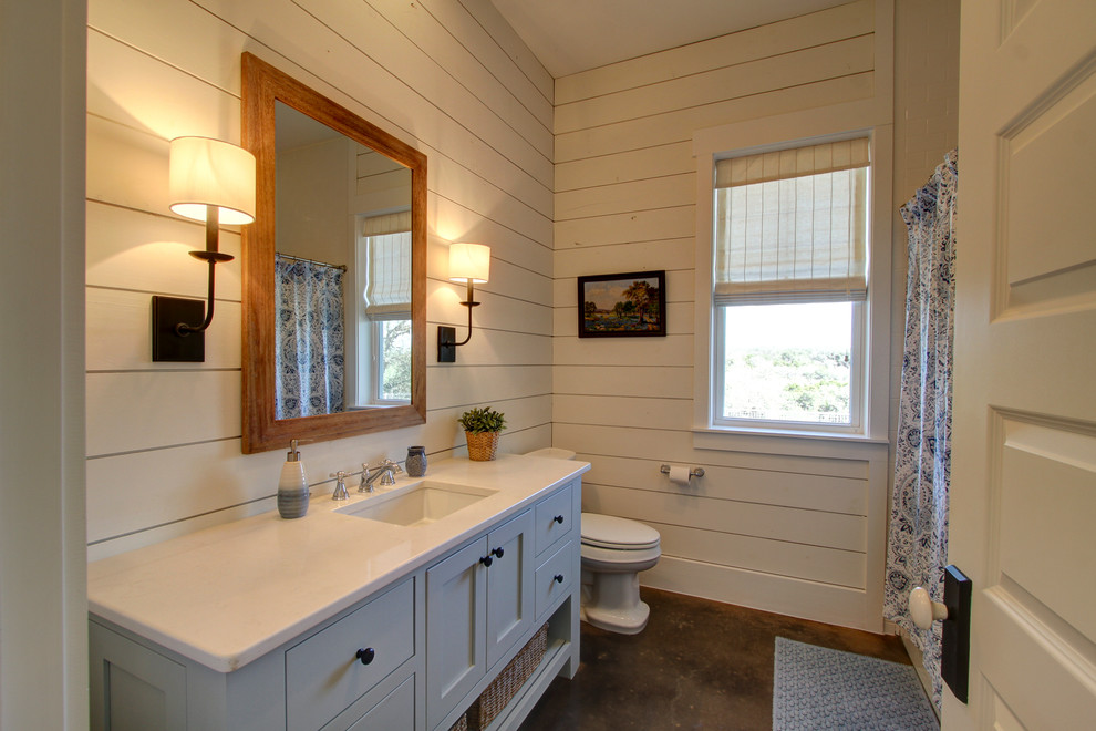 Farmhouse white tile concrete floor drop-in bathtub photo in Austin with shaker cabinets, blue cabinets, a two-piece toilet, white walls, an undermount sink and quartzite countertops