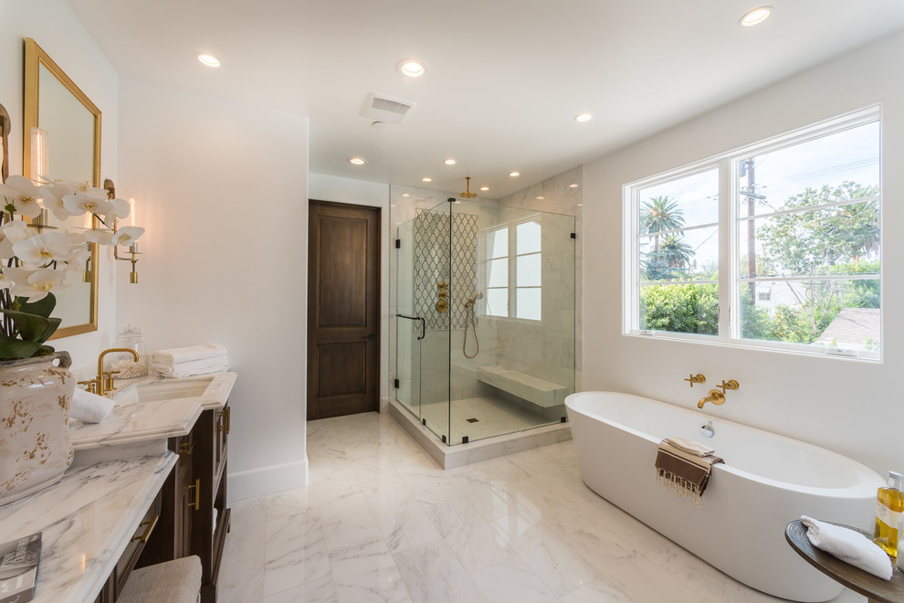 Exempel på ett medelhavsstil beige beige en-suite badrum, med luckor med infälld panel, skåp i mörkt trä, ett fristående badkar, en hörndusch, beige kakel, marmorkakel, vita väggar, marmorgolv, ett undermonterad handfat, marmorbänkskiva, beiget golv och dusch med gångjärnsdörr