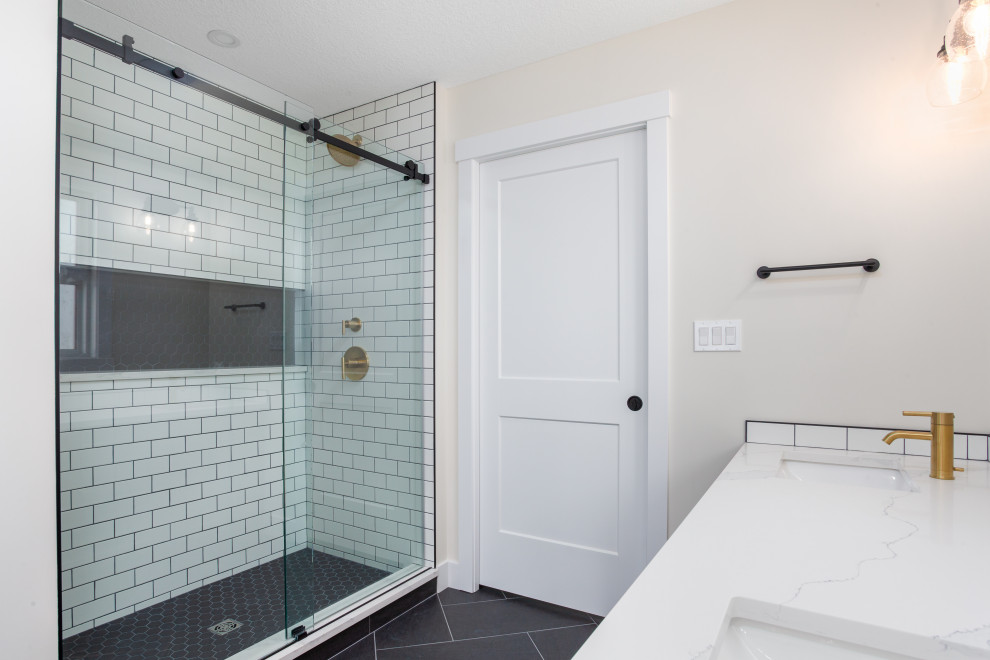 This is an example of a large rural ensuite bathroom in Edmonton with a freestanding bath, a double shower, white tiles, ceramic tiles, white walls, a sliding door, shaker cabinets, medium wood cabinets, a one-piece toilet, porcelain flooring, a submerged sink, engineered stone worktops, black floors and white worktops.