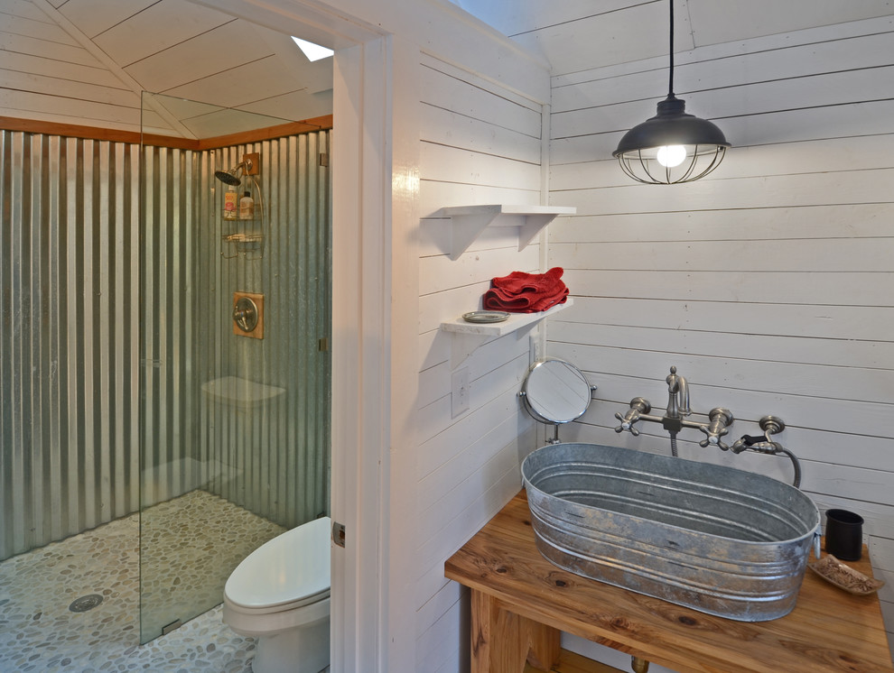 Inredning av ett lantligt brun brunt en-suite badrum, med öppna hyllor, skåp i mellenmörkt trä, en kantlös dusch, en toalettstol med hel cisternkåpa, kakel i småsten, vita väggar, ett fristående handfat, träbänkskiva och klinkergolv i småsten