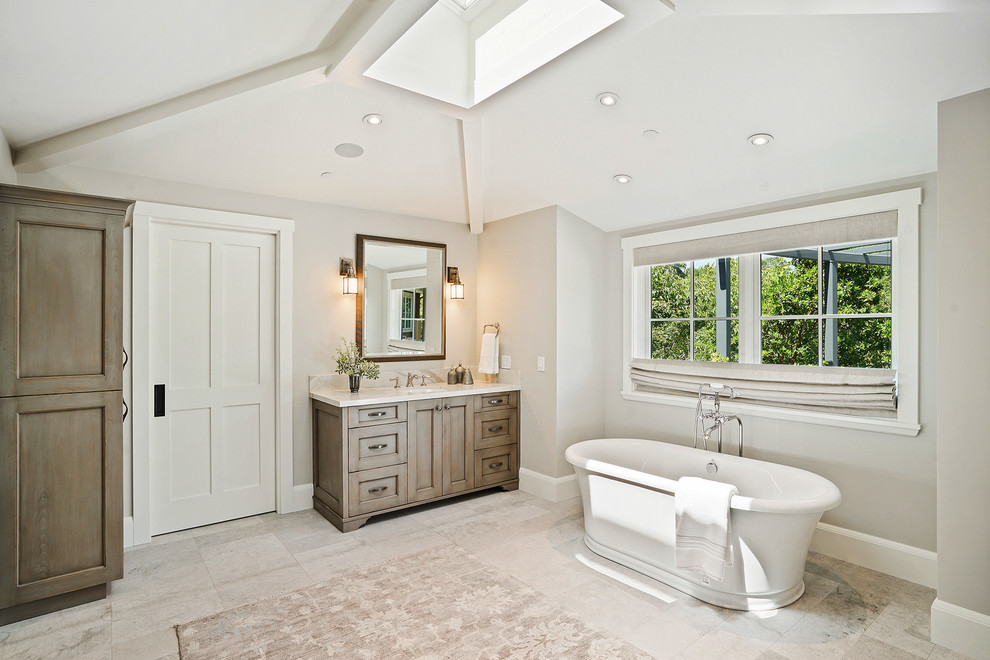 Aménagement d'une grande salle de bain principale campagne en bois brun avec un placard à porte shaker, une baignoire indépendante, un mur gris, un sol en calcaire, un lavabo encastré, un plan de toilette en quartz, un sol gris et un plan de toilette blanc.