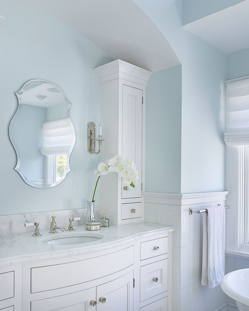 Immagine di una stanza da bagno country con lavabo sottopiano, ante bianche e pareti blu
