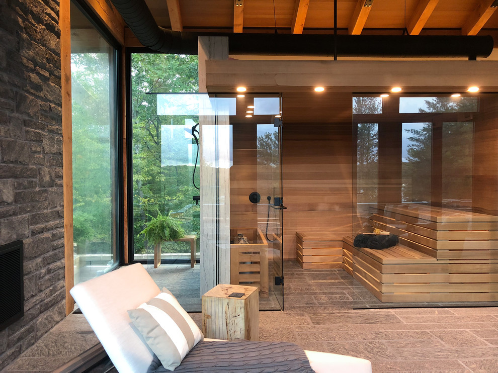 Imagen de sauna campestre grande con suelo gris, ducha a ras de suelo, paredes marrones, ducha con puerta con bisagras y piedra