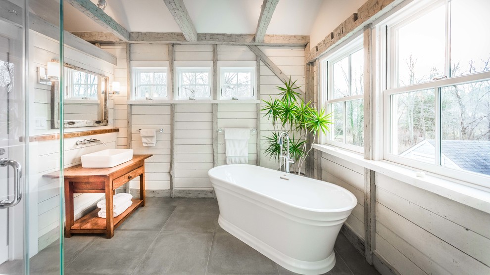 ニューヨークにあるカントリー風のおしゃれな浴室 (中間色木目調キャビネット、置き型浴槽、白い壁、ベッセル式洗面器、木製洗面台、グレーの床、ブラウンの洗面カウンター、フラットパネル扉のキャビネット) の写真
