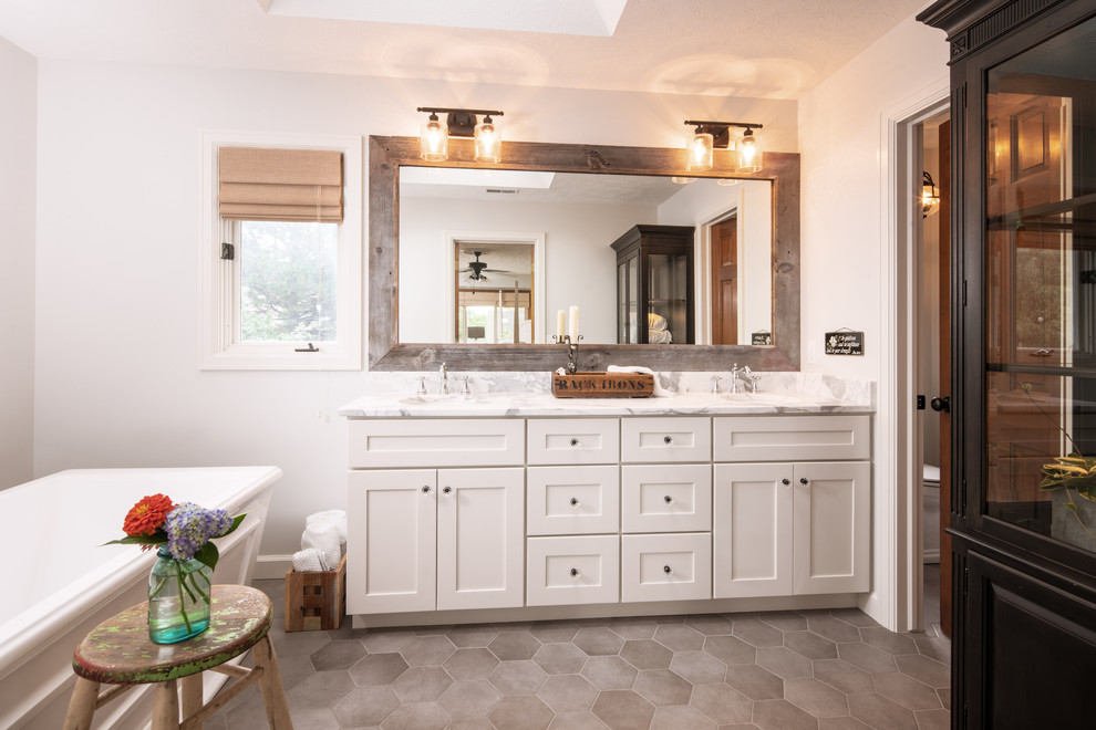 Inspiration for a medium sized country ensuite bathroom in Omaha with shaker cabinets, white cabinets, a freestanding bath, an alcove shower, white tiles, ceramic tiles, white walls, porcelain flooring, a submerged sink, marble worktops, grey floors, a hinged door and white worktops.