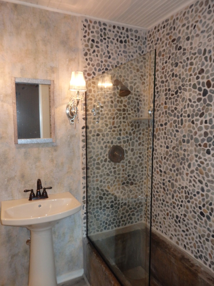 Foto på ett litet lantligt badrum med dusch, med en toalettstol med separat cisternkåpa, flerfärgad kakel, kakel i småsten, flerfärgade väggar, vinylgolv, ett piedestal handfat och beiget golv