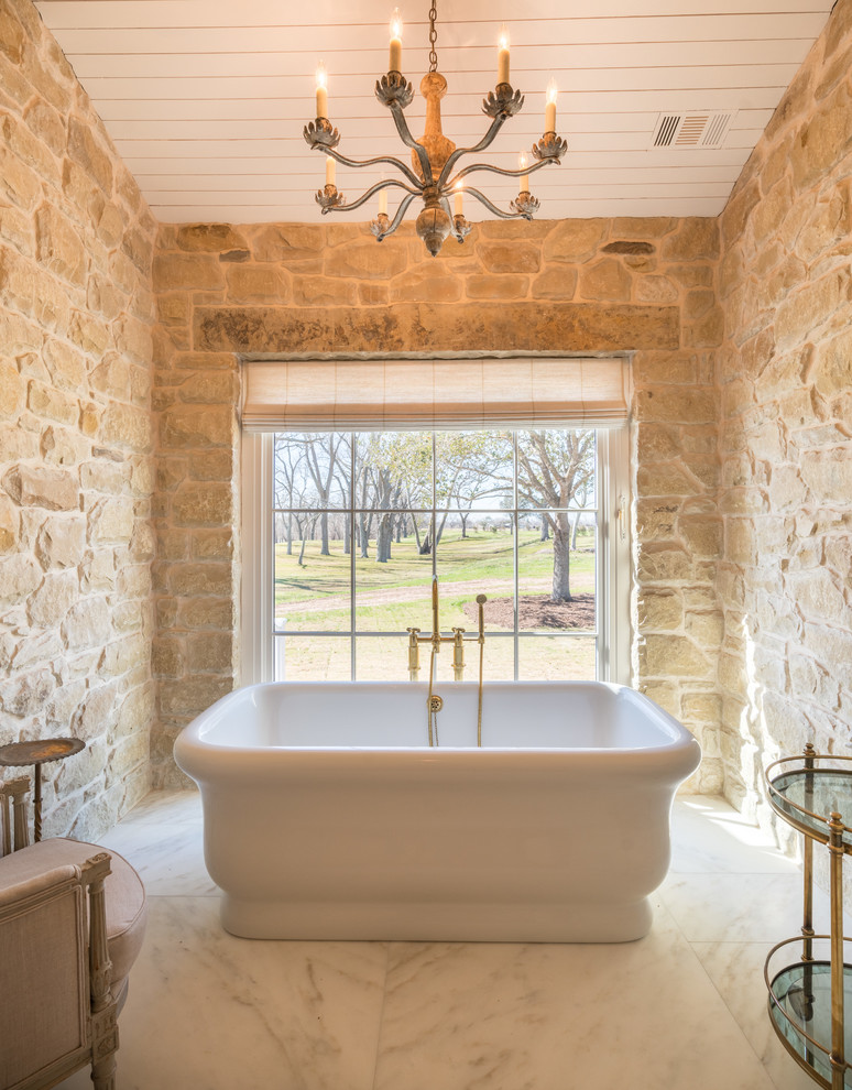 Cette image montre une salle de bain rustique avec une baignoire indépendante, un carrelage beige, un carrelage de pierre, un mur beige et un sol blanc.