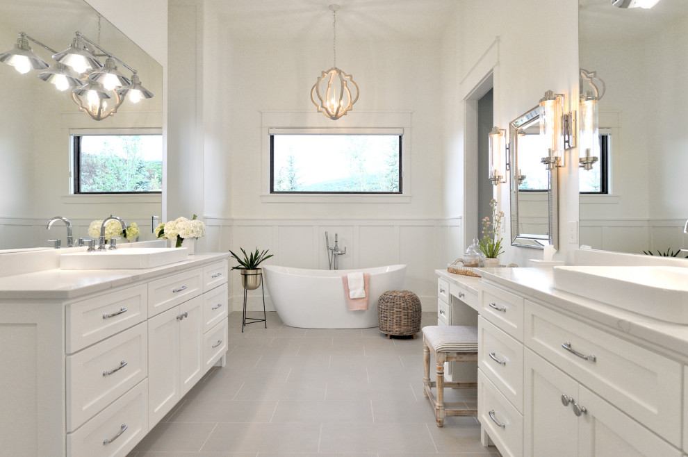 На фото: главная ванная комната в стиле неоклассика (современная классика) с фасадами в стиле шейкер, белыми фасадами, отдельно стоящей ванной, белыми стенами, настольной раковиной, серым полом и белой столешницей