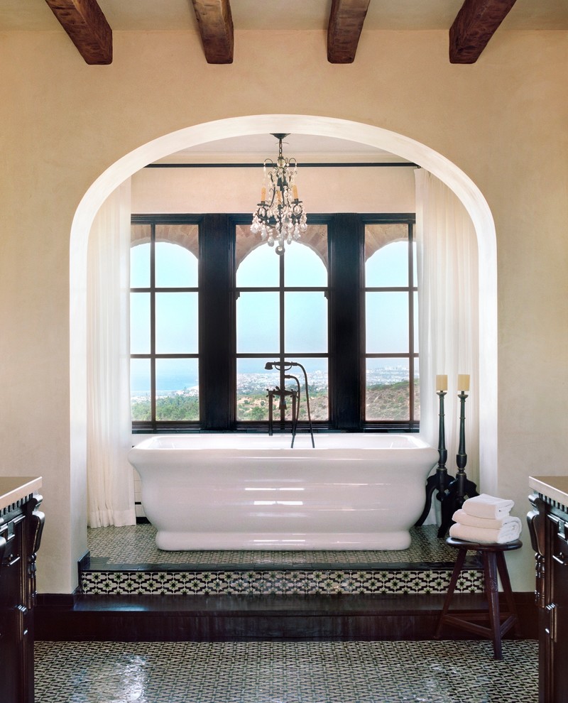 Klassisk inredning av ett stort en-suite badrum, med ett fristående badkar, en toalettstol med separat cisternkåpa, beige väggar, mosaikgolv och flerfärgat golv