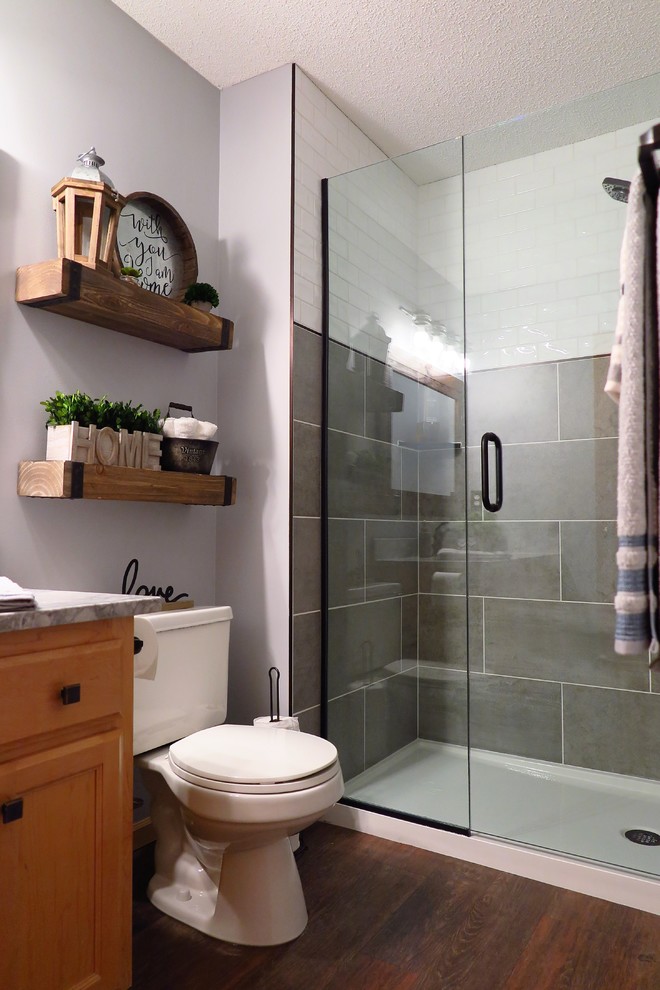 Inspiration for a medium sized farmhouse shower room bathroom in Minneapolis with shaker cabinets, light wood cabinets, an alcove shower, a two-piece toilet, white tiles, ceramic tiles, grey walls, vinyl flooring, a submerged sink, marble worktops, brown floors, a hinged door and white worktops.