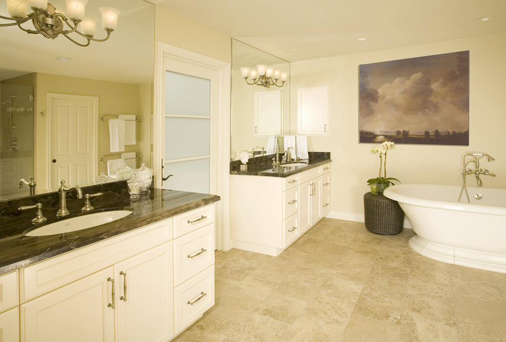 Klassisk inredning av ett mellanstort en-suite badrum, med skåp i shakerstil, vita skåp, ett fristående badkar, beige väggar, travertin golv, ett undermonterad handfat, marmorbänkskiva och brunt golv