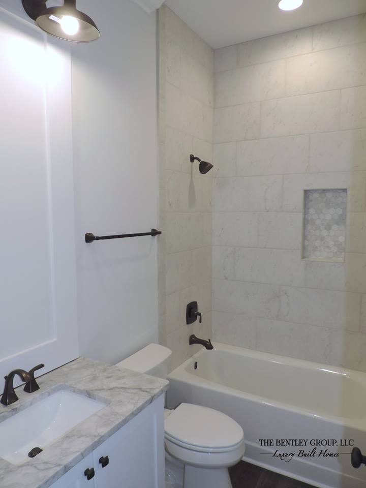 Exempel på ett mellanstort lantligt badrum, med luckor med infälld panel, vita skåp, ett badkar i en alkov, en dusch/badkar-kombination, vit kakel, marmorkakel, vita väggar, mörkt trägolv, ett undermonterad handfat, marmorbänkskiva, brunt golv och dusch med duschdraperi