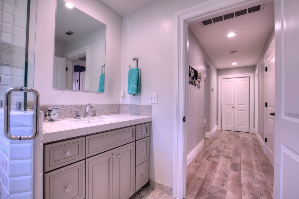 На фото: ванная комната среднего размера в классическом стиле с плоскими фасадами, серыми фасадами, раздельным унитазом, белой плиткой, керамической плиткой, белыми стенами, полом из травертина, врезной раковиной, столешницей из искусственного кварца и серым полом