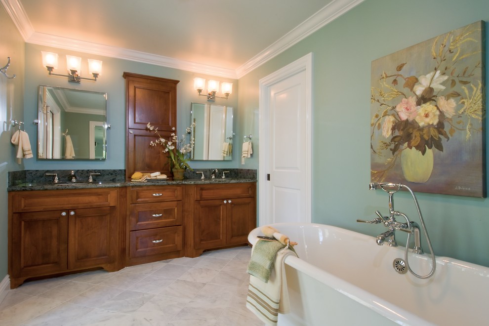 Aménagement d'une grande salle de bain principale classique en bois brun avec un placard avec porte à panneau encastré, une baignoire indépendante, un mur bleu, un sol en calcaire, un lavabo encastré, un plan de toilette en granite et un sol blanc.