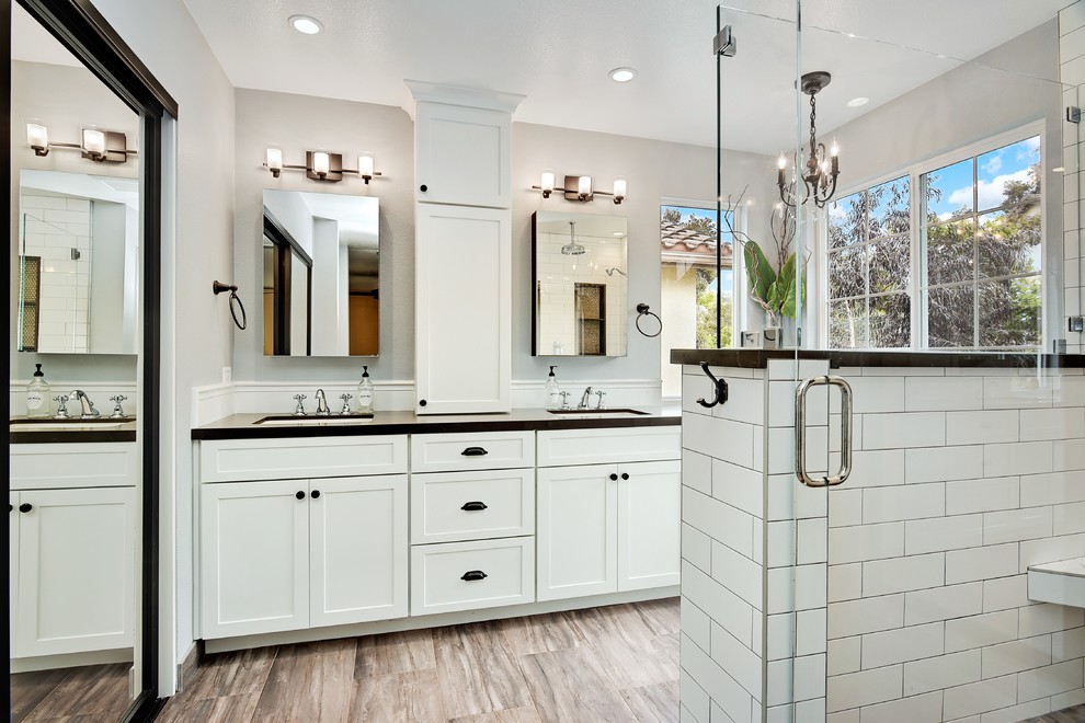 Example of a mid-sized farmhouse master white tile and ceramic tile ceramic tile and brown floor corner shower design in San Diego with shaker cabinets, white cabinets, a one-piece toilet, gray walls, an undermount sink, quartz countertops, a hinged shower door and brown countertops