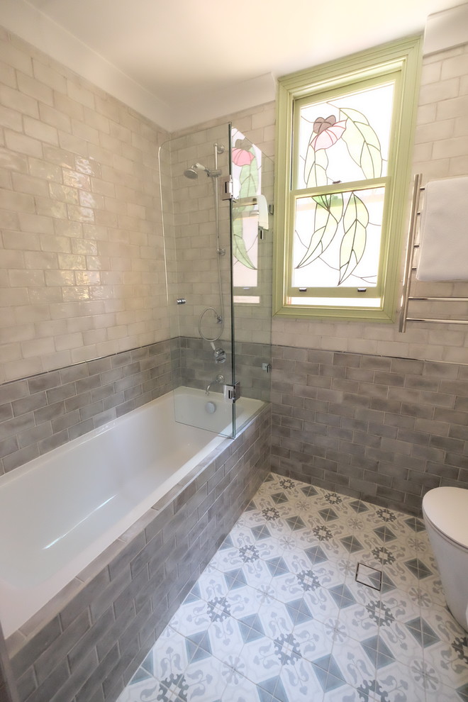 На фото: маленькая ванная комната в средиземноморском стиле с плоскими фасадами, белыми фасадами, накладной ванной, душем над ванной, инсталляцией, серой плиткой, плиткой кабанчик, серыми стенами, полом из керамогранита, монолитной раковиной, столешницей из искусственного камня, разноцветным полом, душем с распашными дверями и белой столешницей для на участке и в саду