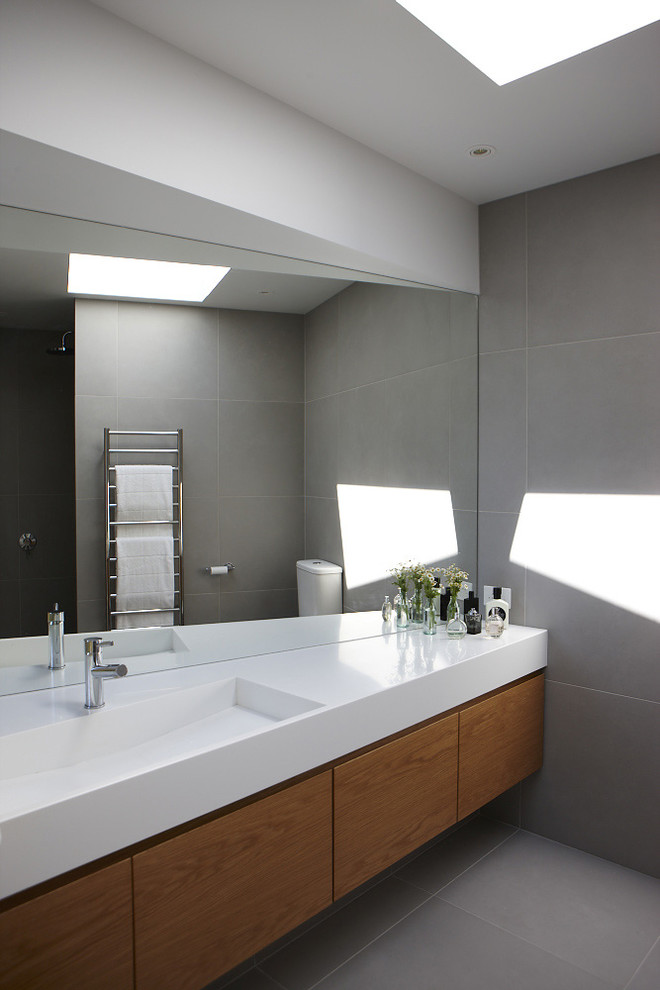 Esempio di una stanza da bagno contemporanea con lavabo integrato, ante lisce, ante in legno scuro e piastrelle grigie