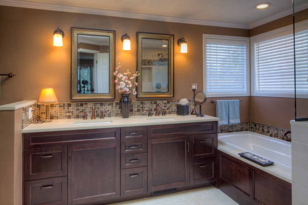 Cette image montre une salle de bain principale traditionnelle en bois foncé de taille moyenne avec un placard avec porte à panneau encastré, une baignoire posée, un carrelage marron, un carrelage en pâte de verre, un mur marron, un lavabo encastré, un plan de toilette beige, un sol en carrelage de porcelaine, un plan de toilette en quartz modifié, un sol beige, meuble double vasque et meuble-lavabo encastré.