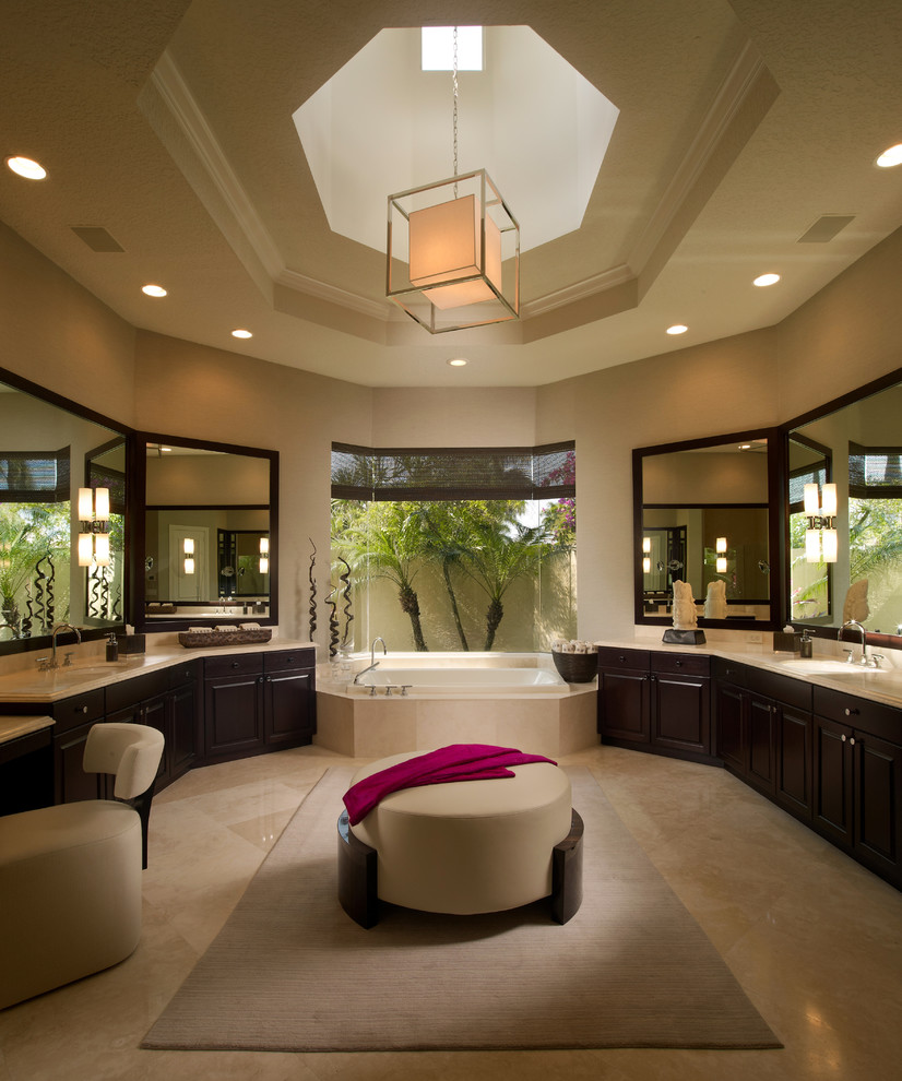 Example of a trendy beige tile beige floor drop-in bathtub design in Miami with an undermount sink, raised-panel cabinets and dark wood cabinets