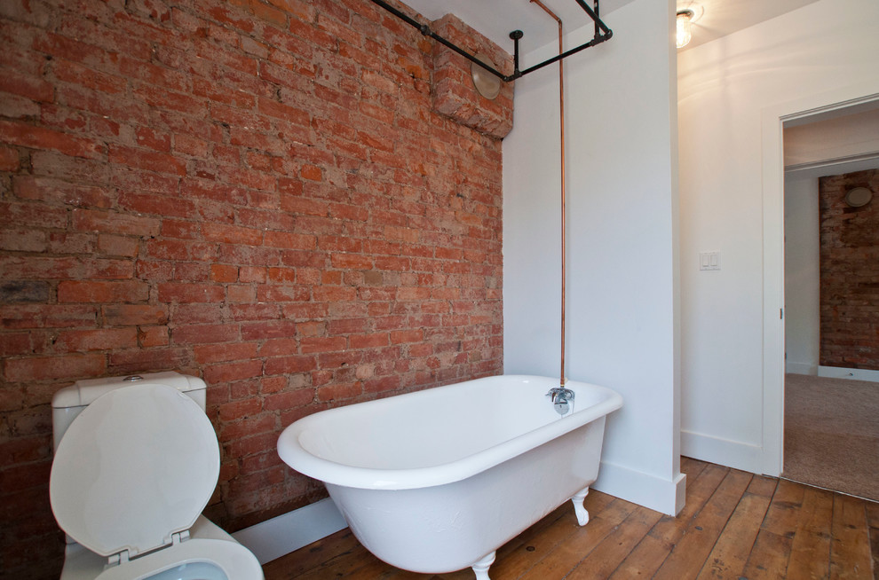 Aménagement d'une salle de bain industrielle de taille moyenne avec une baignoire sur pieds, un combiné douche/baignoire, un mur blanc et un sol en bois brun.