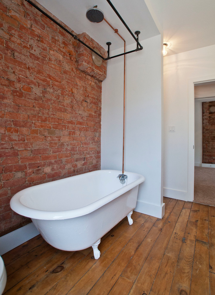 Idee per una stanza da bagno industriale di medie dimensioni con vasca con piedi a zampa di leone, vasca/doccia, pareti bianche e pavimento in legno massello medio