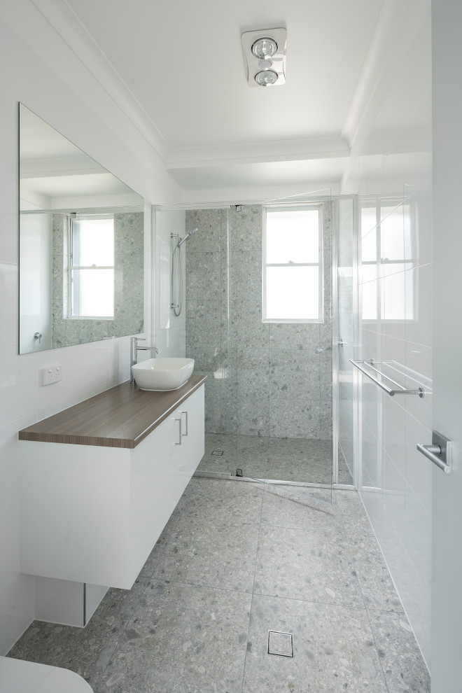 Maritim inredning av ett brun brunt en-suite badrum, med en toalettstol med hel cisternkåpa, vit kakel, porslinskakel, grå väggar, terrazzogolv, laminatbänkskiva och grått golv