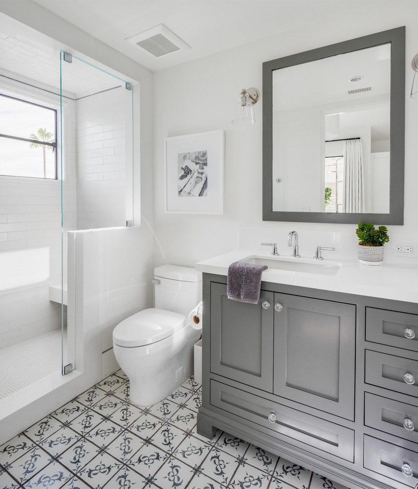 This is an example of a coastal shower room bathroom in Orange County with shaker cabinets, grey cabinets, an alcove shower, a one-piece toilet, white tiles, metro tiles, white walls, a submerged sink, multi-coloured floors and white worktops.