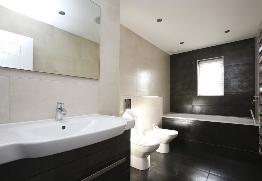 This is an example of a large classic family bathroom in Essex with flat-panel cabinets, black cabinets, a built-in bath, a two-piece toilet, black tiles, stone slabs, beige walls, porcelain flooring and a wall-mounted sink.