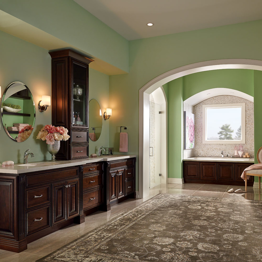 Example of a huge classic master beige floor alcove bathtub design in Other with raised-panel cabinets, dark wood cabinets, green walls and an undermount sink