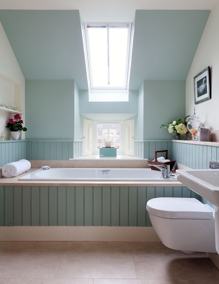 Стильный дизайн: ванная комната в стиле неоклассика (современная классика) с подвесной раковиной, накладной ванной, инсталляцией, синими стенами, каменной плиткой, полом из известняка и бежевым полом - последний тренд