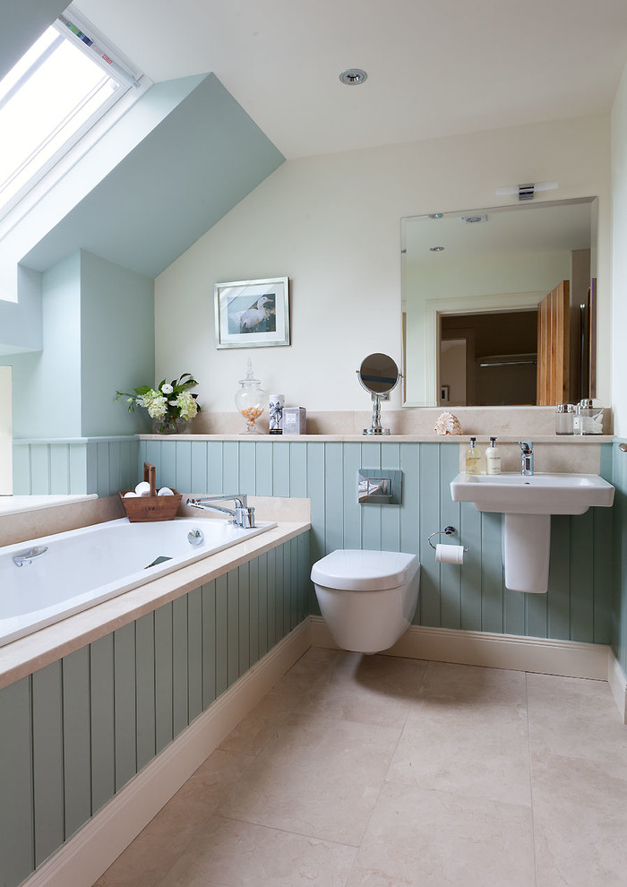 Modelo de cuarto de baño marinero con sanitario de una pieza, paredes azules, suelo de piedra caliza, lavabo suspendido y encimera de piedra caliza