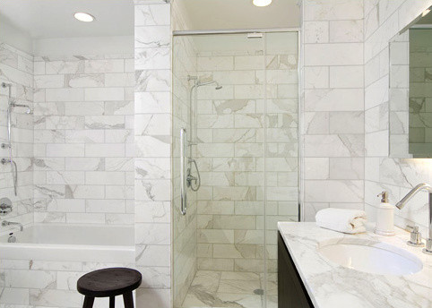 Cette image montre une salle de bain minimaliste en bois foncé de taille moyenne avec un lavabo encastré, un placard à porte plane, un plan de toilette en marbre, une baignoire posée, un carrelage blanc, un carrelage de pierre, un mur blanc, un sol en marbre et WC à poser.