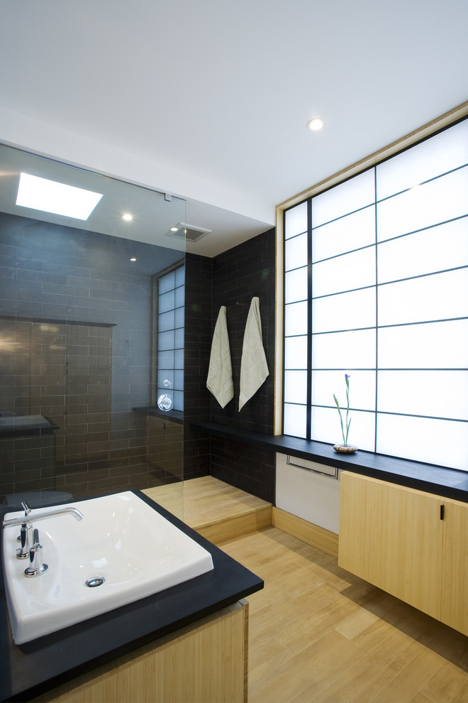 Réalisation d'une salle de bain asiatique en bois clair avec un lavabo posé, un placard à porte plane et un carrelage gris.