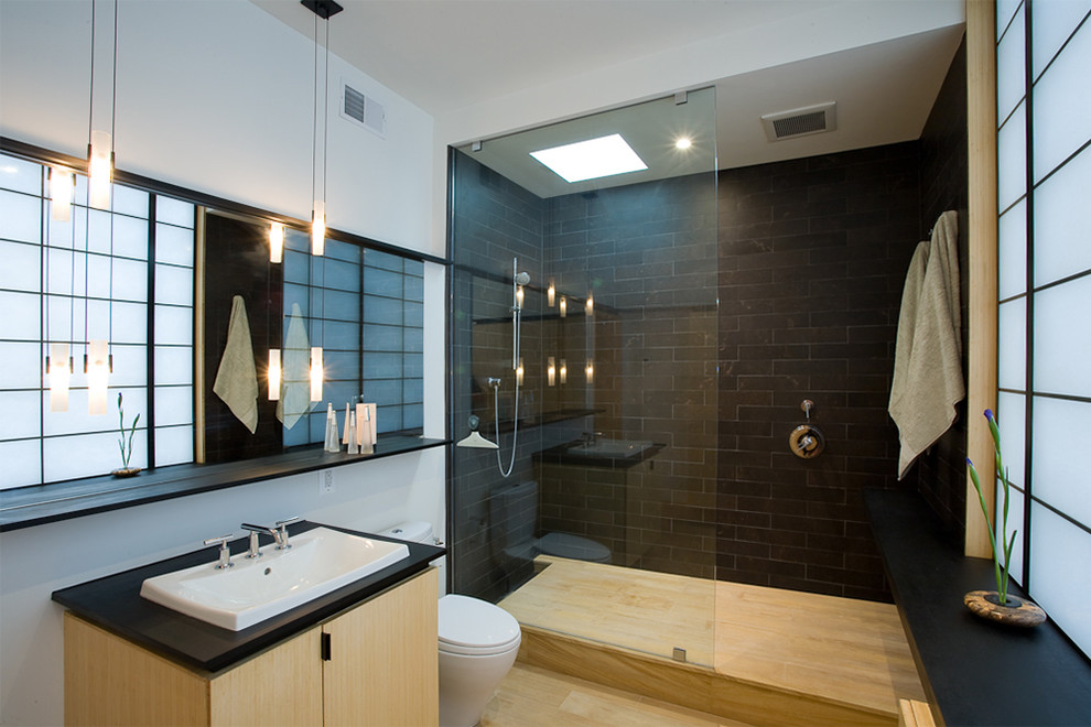 Foto på ett funkis badrum, med ett nedsänkt handfat, släta luckor, skåp i ljust trä, en dusch i en alkov, en toalettstol med separat cisternkåpa och svart kakel