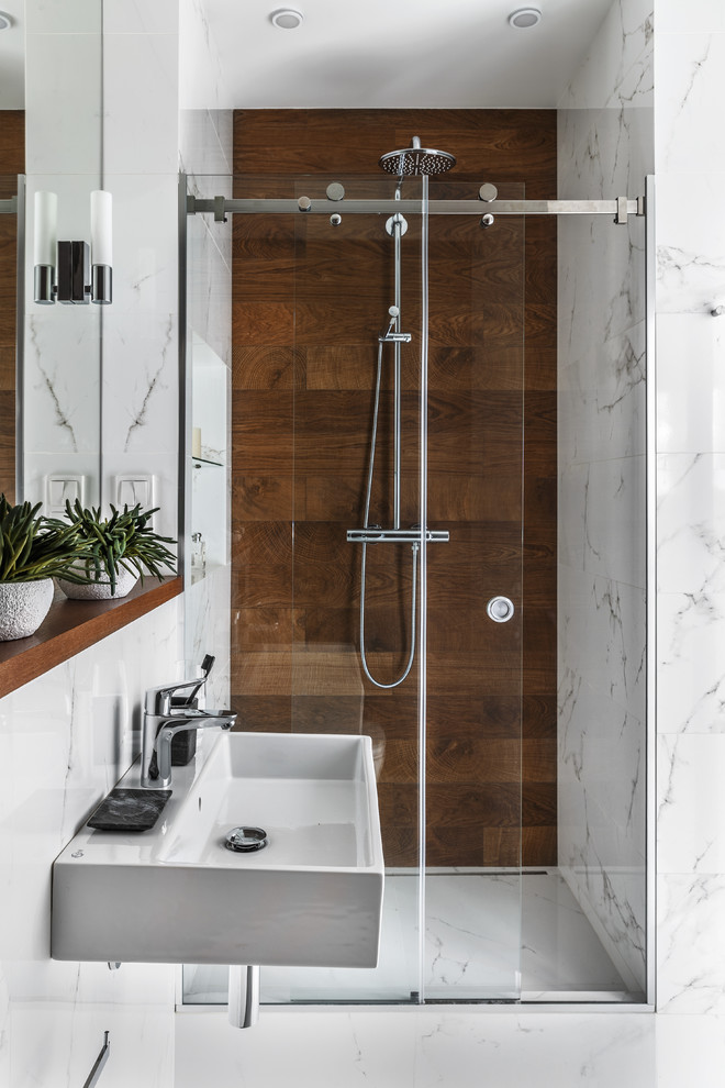 Inredning av ett modernt badrum med dusch, med en dusch i en alkov, brun kakel, vit kakel, ett väggmonterat handfat, dusch med skjutdörr, marmorgolv och vitt golv