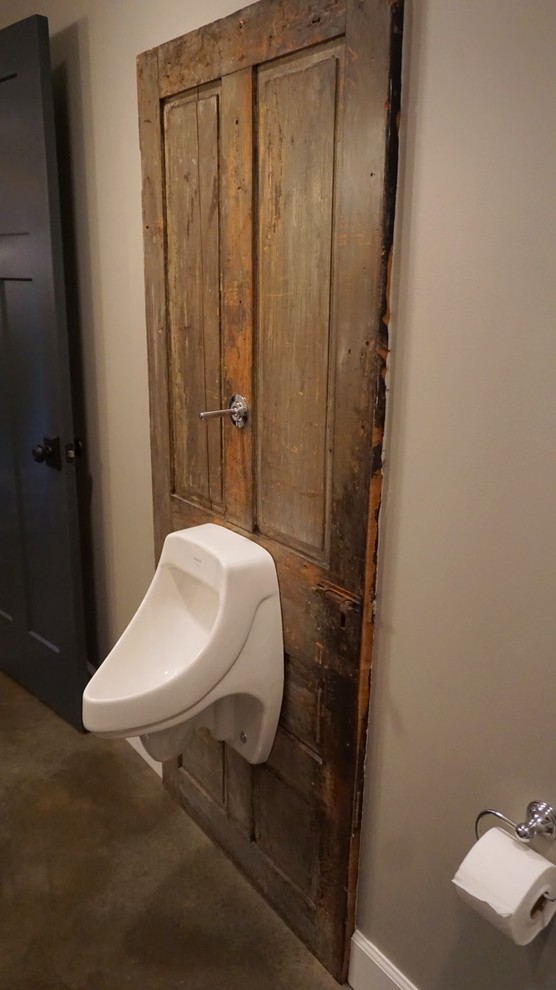 Inredning av ett modernt mellanstort badrum, med ett avlångt handfat, öppna hyllor, blå skåp, träbänkskiva, ett badkar i en alkov, en dusch/badkar-kombination, ett urinoar, grå väggar och betonggolv