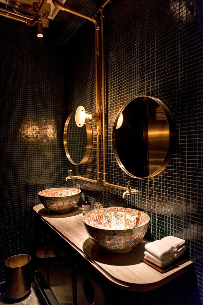 На фото: ванная комната в стиле лофт с коричневыми фасадами, черной плиткой, плиткой мозаикой, настольной раковиной, столешницей из дерева, коричневой столешницей и плоскими фасадами с
