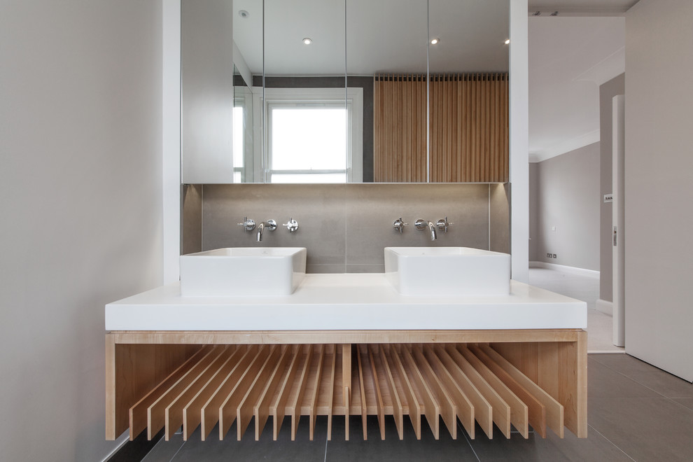 This is an example of a medium sized contemporary ensuite bathroom in London with flat-panel cabinets, light wood cabinets, a freestanding bath, a walk-in shower, a one-piece toilet, grey tiles, porcelain tiles, grey walls, porcelain flooring, a console sink and quartz worktops.