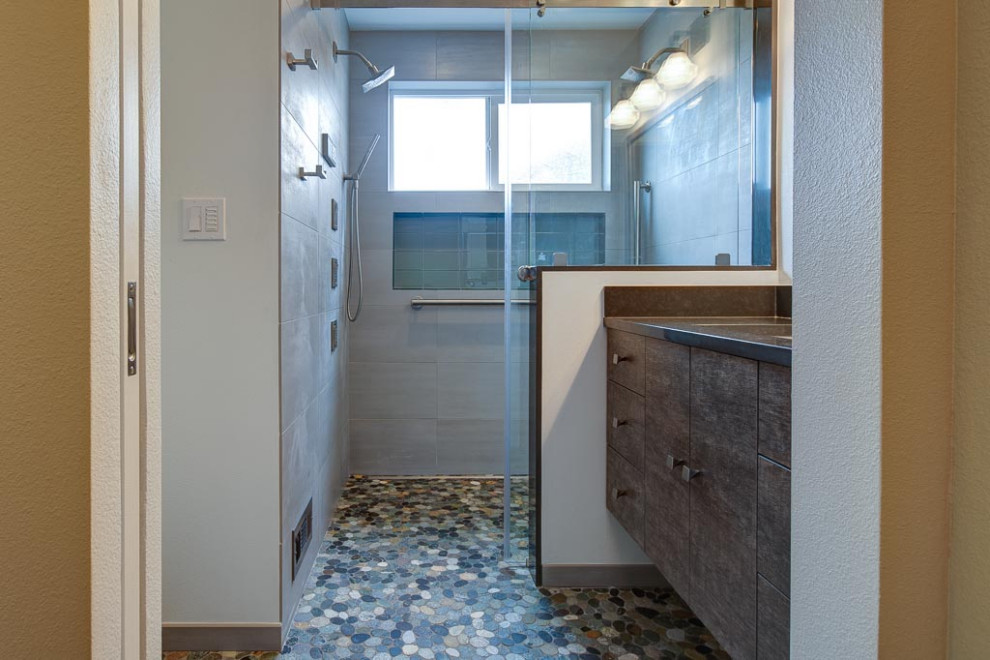 Modern inredning av ett litet grå grått badrum med dusch, med en kantlös dusch, en vägghängd toalettstol, grå kakel, vita väggar, klinkergolv i småsten, flerfärgat golv och dusch med skjutdörr