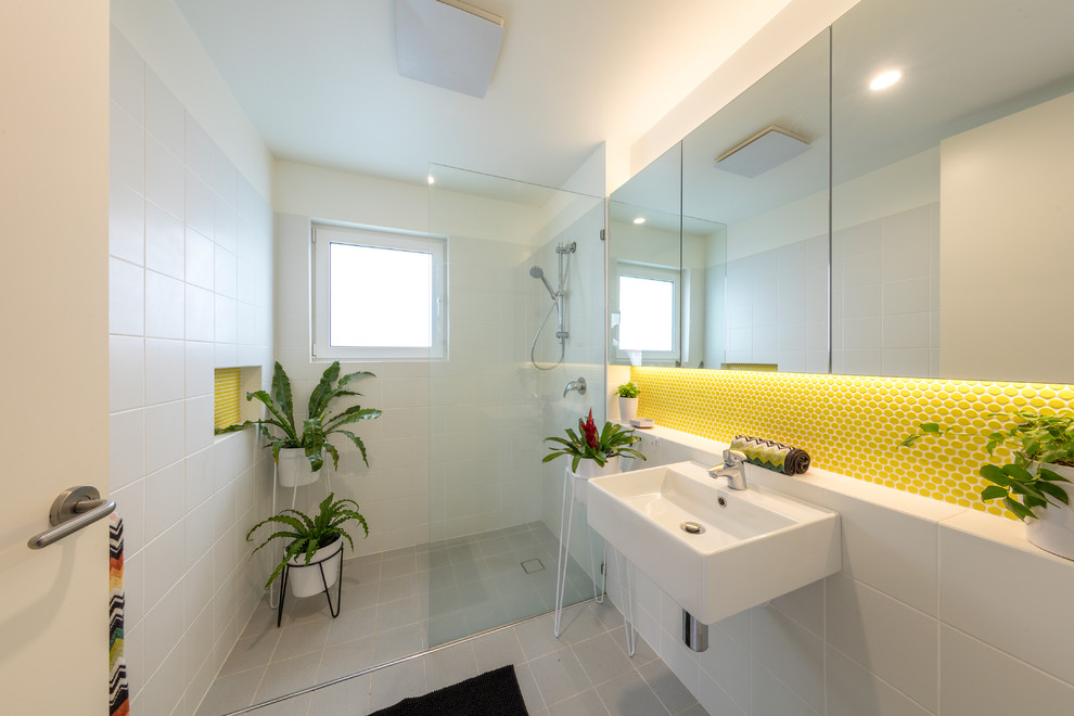 Modern inredning av ett litet badrum, med en kantlös dusch, gul kakel, keramikplattor, vita väggar, cementgolv, ett väggmonterat handfat, grått golv och med dusch som är öppen