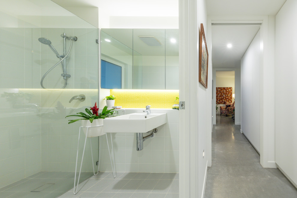 Idéer för att renovera ett litet funkis badrum, med luckor med glaspanel, en kantlös dusch, en toalettstol med hel cisternkåpa, gul kakel, keramikplattor, vita väggar, cementgolv, ett väggmonterat handfat, grått golv och med dusch som är öppen
