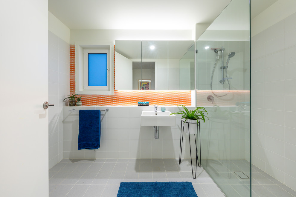 Inredning av ett modernt litet badrum, med en kantlös dusch, grå kakel, ett väggmonterat handfat, grått golv och med dusch som är öppen