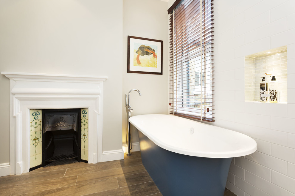Modern bathroom in London with a freestanding bath, white tiles, metro tiles, white walls, medium hardwood flooring and a chimney breast.