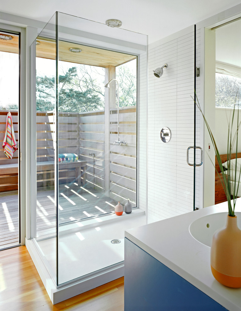 Modelo de cuarto de baño marinero con ducha esquinera, baldosas y/o azulejos blancos, suelo de madera en tonos medios y ventanas