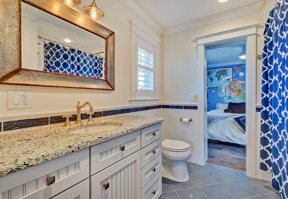 This is an example of a medium sized coastal family bathroom in New York with recessed-panel cabinets, white cabinets, a one-piece toilet, white tiles, ceramic flooring, recycled glass worktops, an alcove bath, a shower/bath combination, ceramic tiles, white walls and a submerged sink.
