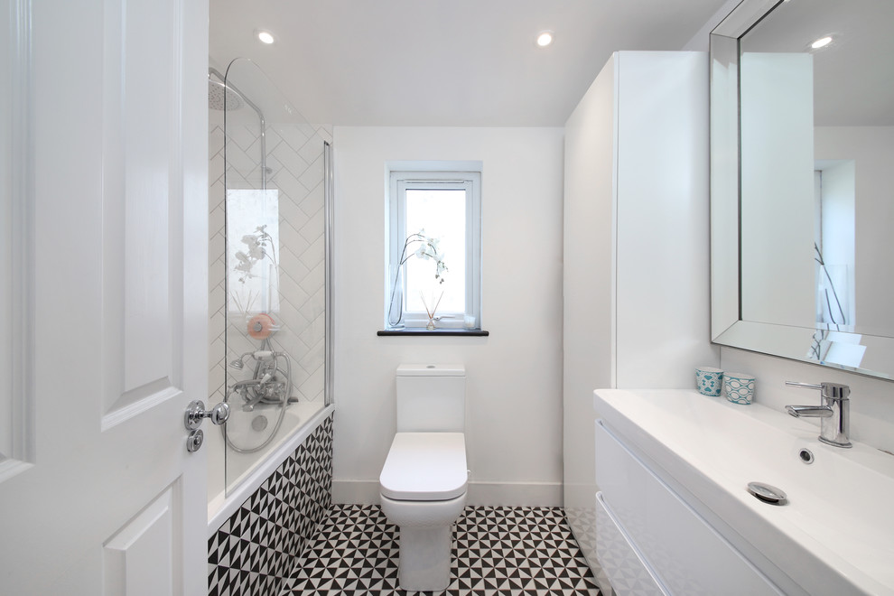 Diseño de cuarto de baño azulejo de dos tonos escandinavo con armarios con paneles lisos, puertas de armario blancas, bañera empotrada, combinación de ducha y bañera, sanitario de dos piezas, paredes blancas y suelo multicolor