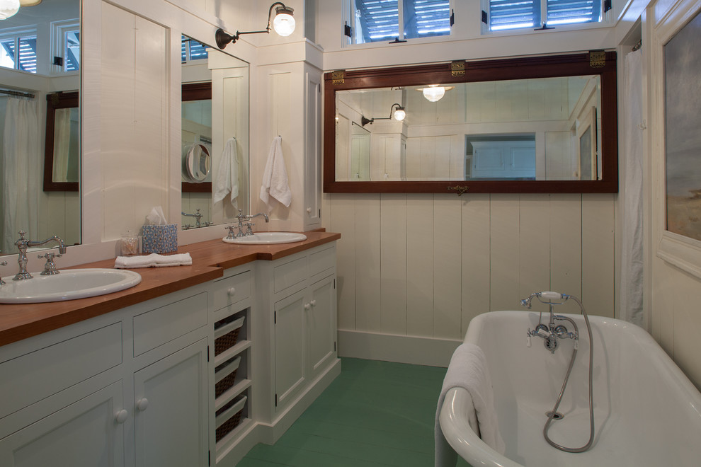 Modelo de cuarto de baño costero con lavabo encastrado, bañera exenta, encimera de madera, suelo verde y encimeras marrones