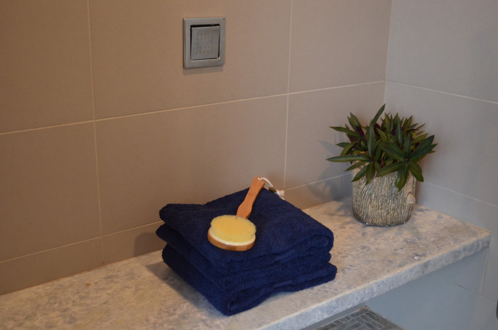 Пример оригинального дизайна: главная ванная комната в современном стиле с врезной раковиной, плоскими фасадами, фасадами цвета дерева среднего тона, столешницей из оникса, отдельно стоящей ванной, двойным душем, унитазом-моноблоком, серой плиткой, керамогранитной плиткой, серыми стенами и полом из керамогранита